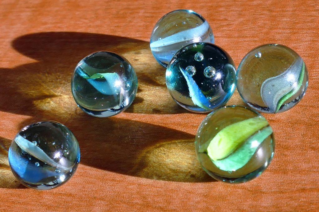 A vivid collection of glass marbles casting colorful reflections on a wooden surface.